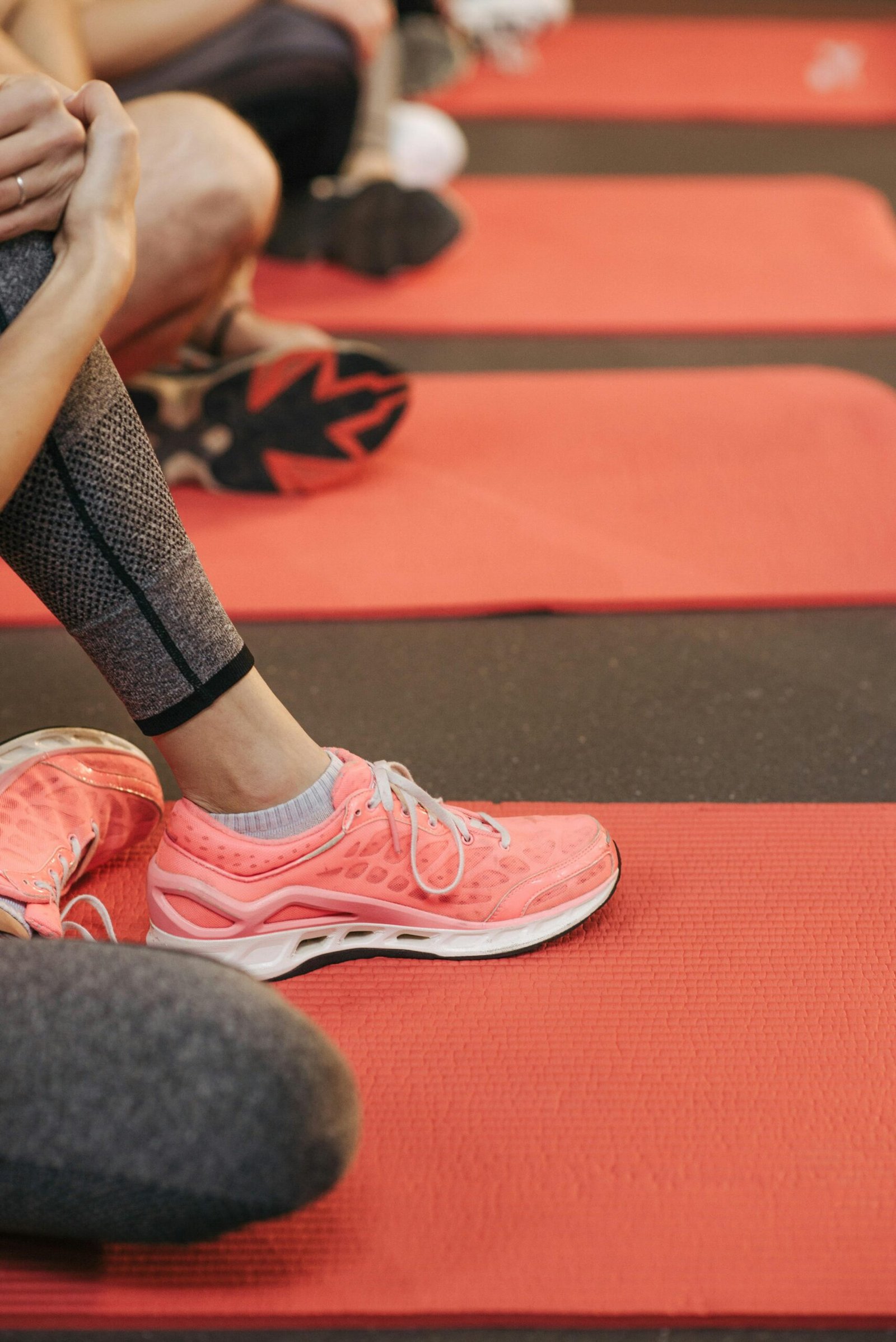 Close-up photo of athletes in leggings and sneakers on red yoga mats.